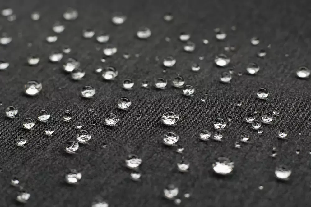 Kapljice vode na temni vodoodbojni tkanini, ki prikazujejo odpornost materiala na dež in odvečno vlago.