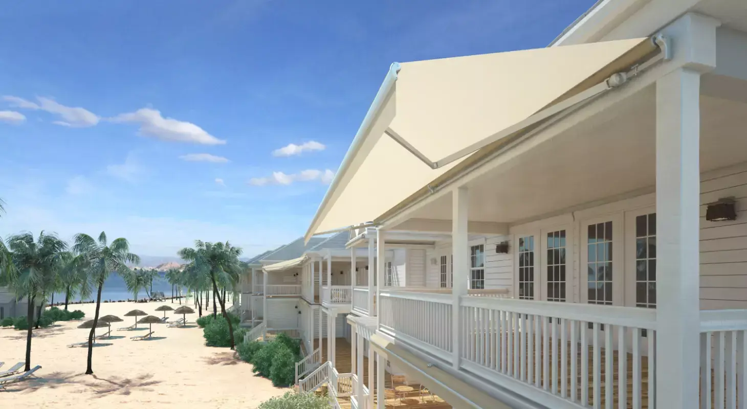 Bež zložljiva tenda na balkonu obalne hiše s pogledom na peščeno plažo in palme.