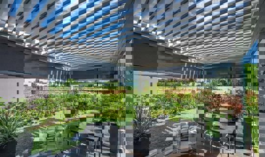 Moderna bioklimatska pergola z lamelami, senčili in steklenimi stenami na vrtni terasi s pogledom na naravo.