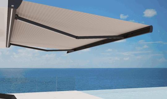 Odprta kasetna tenda s črtastim platnom in raztegljivimi rokami v črni barvi, nameščena na fasado z razgledom na morje.