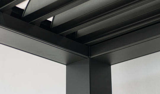 Bližnji posnetek notranjega vogala aluminijaste konstrukcije bioklimatske pergole v črni barvi.