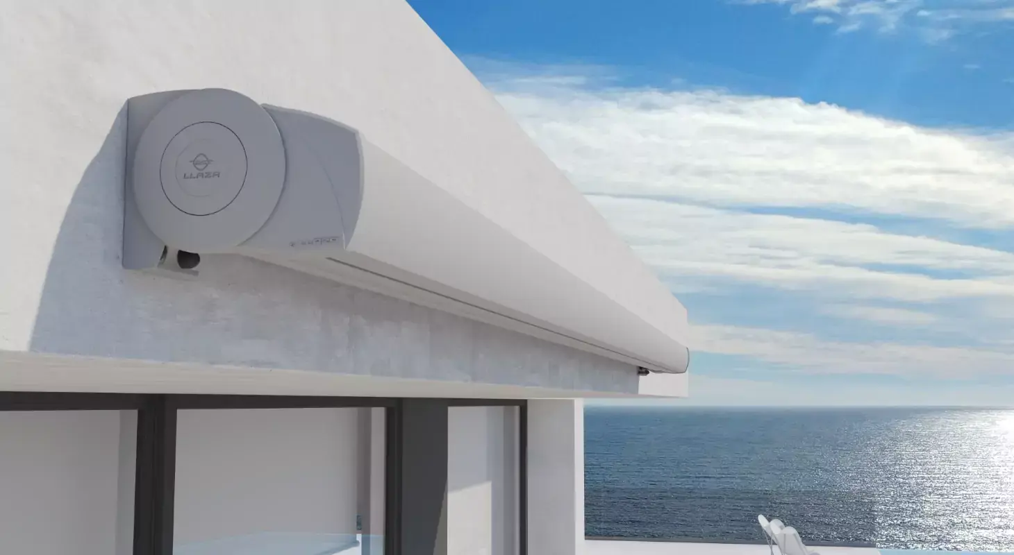 Zaprta kasetna tenda blagovne znamke Llaza, nameščena na sodobni stavbi ob morju pod modrim nebom s svetlimi oblaki.